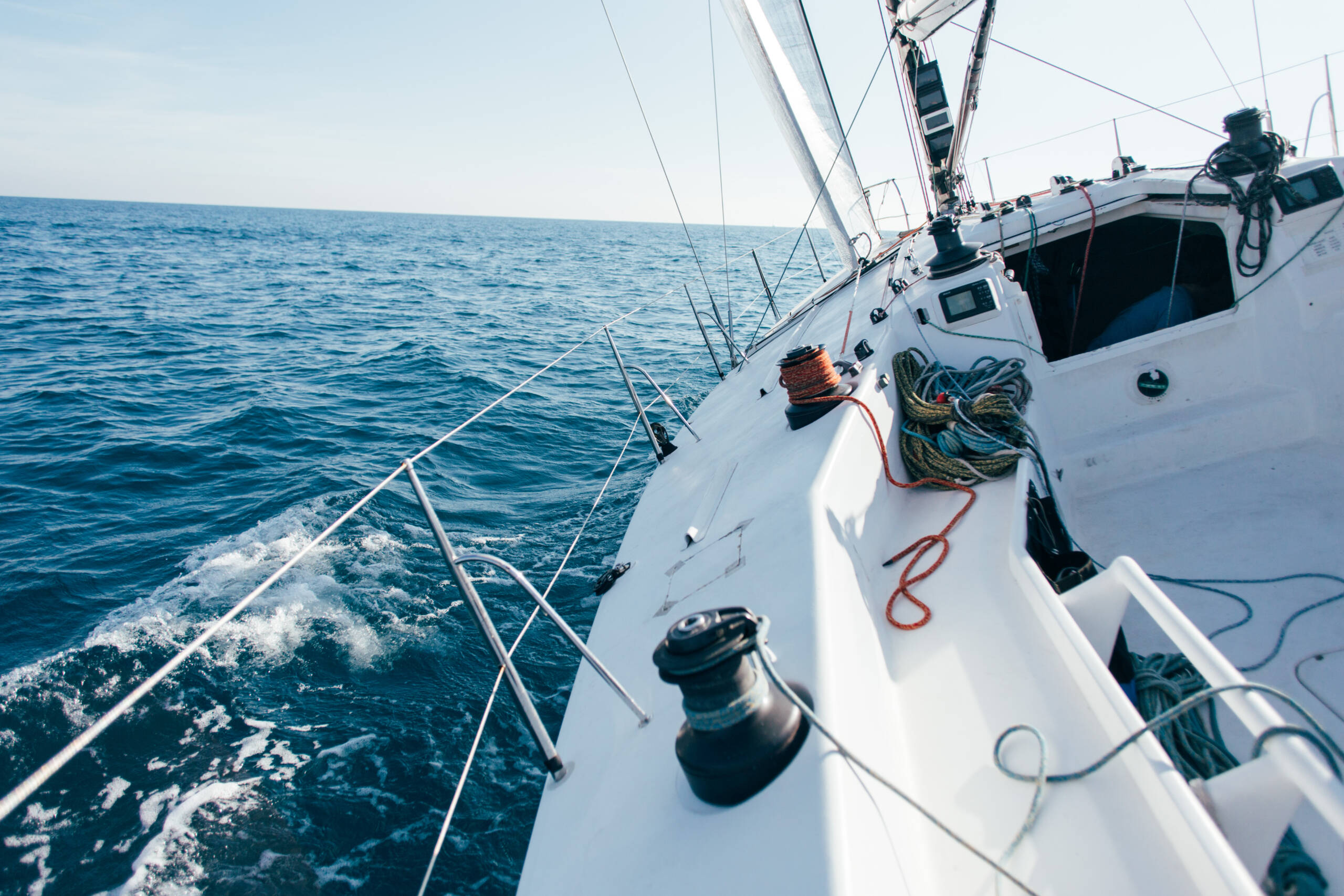 Deck of professional sailboat or racing yacht during competition on sunny and windy summer day, moving fast through waves and water, with spinnaker up, and ropes tied around winch