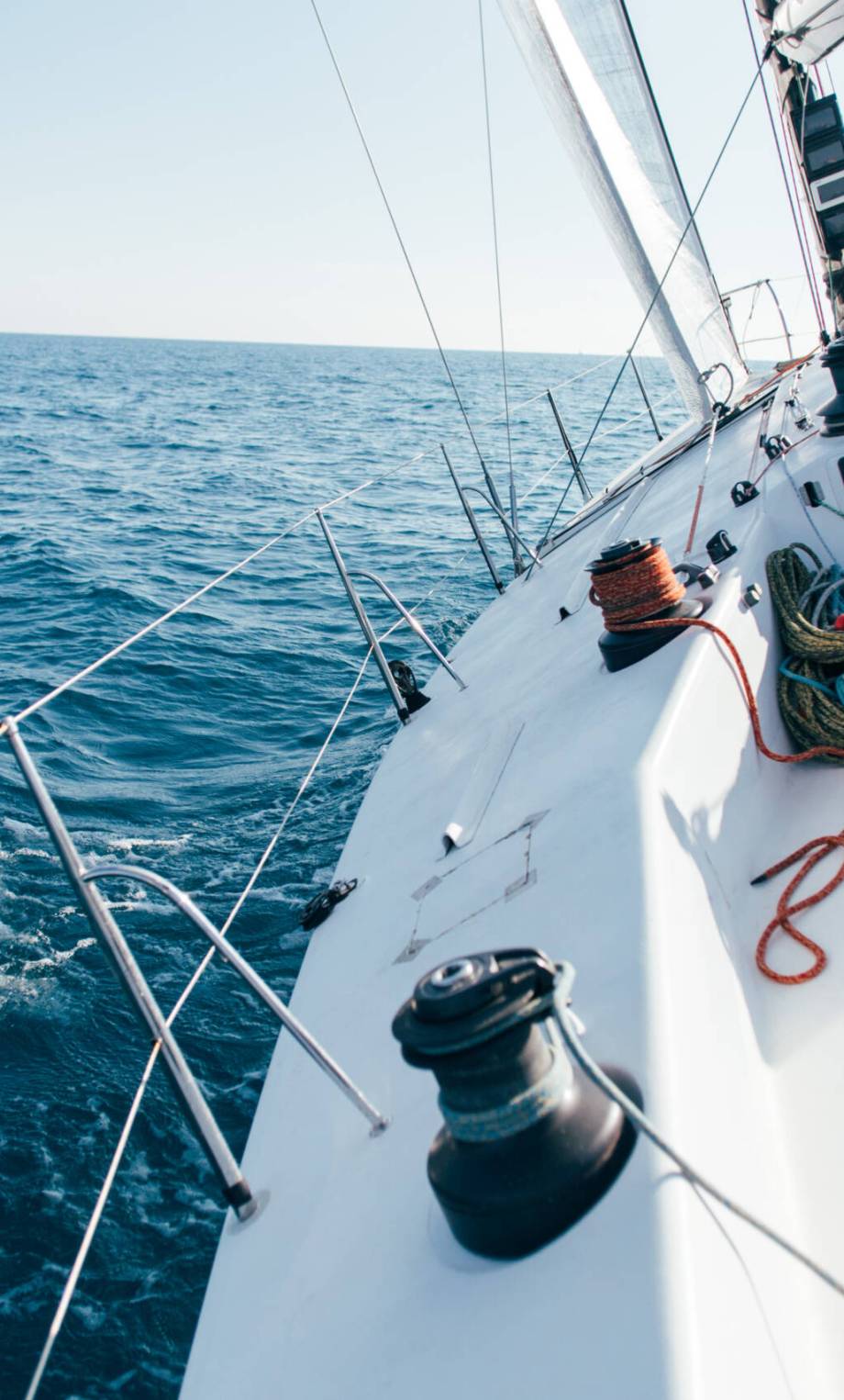 Deck of professional sailboat or racing yacht during competition on sunny and windy summer day, moving fast through waves and water, with spinnaker up, and ropes tied around winch